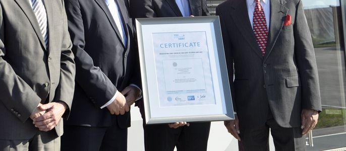 Vier Männer in Anzügen mit einem Zertifikat von "TÜV PROFICERT in der Hand".